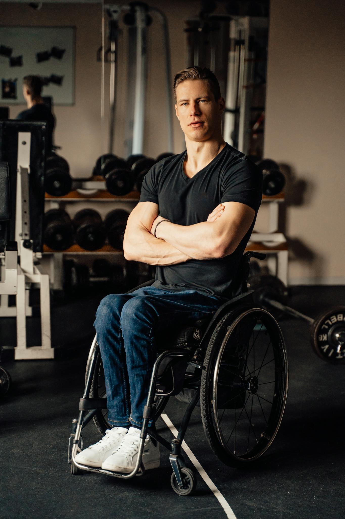 Man in wheelchair confidently poses in a modern gym setting.